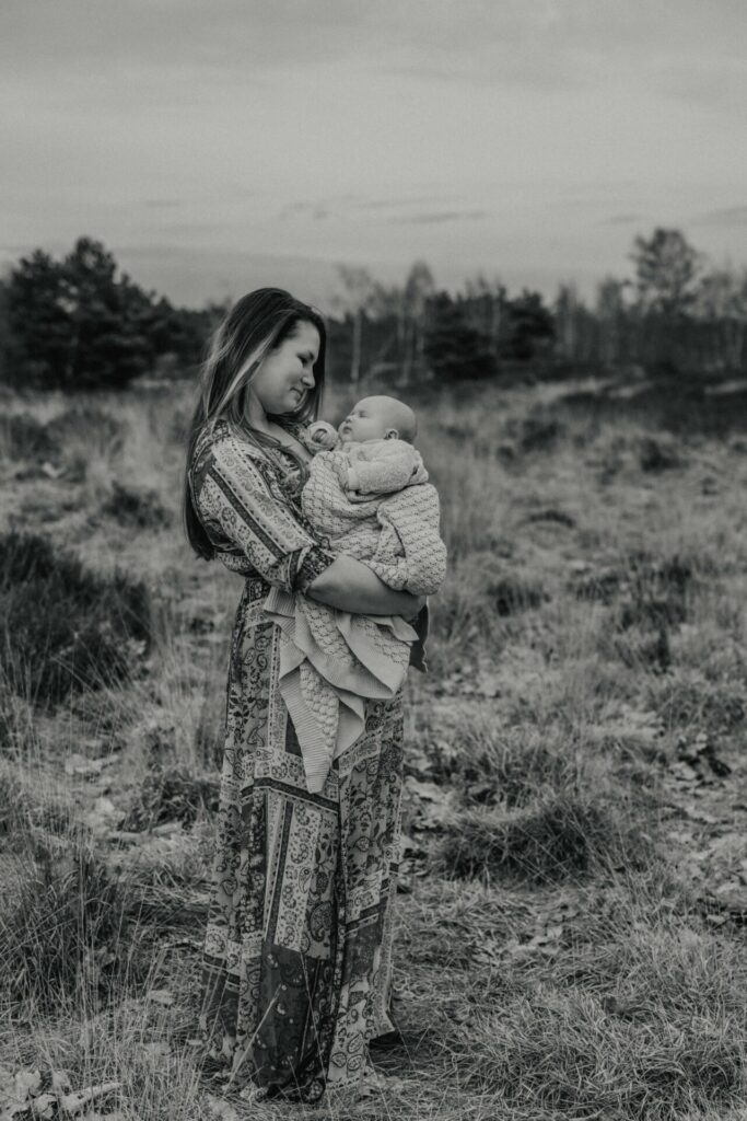 Mama met kleine baby, gewikkeld in een deken buiten op de heide tijdens een newbornshoot
